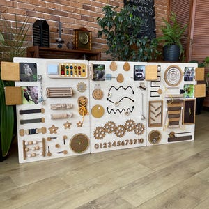 Könnte beinhalten: Eine große Holz-Aktivitätstafel mit mehreren Paneelen, die interaktive Elemente wie Zahnräder, Riegel und Perlen aufweist. Enthält Tierillustrationen und ist für pädagogisches Spielen und sensorische Erkundung konzipiert.