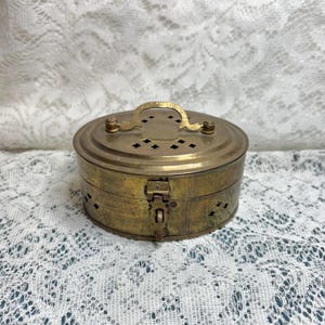 May include: A vintage brass oval box with a hinged lid and a small handle. The box has decorative cutouts and a clasp closure. The brass has a tarnished, aged appearance, suggesting it is an antique or vintage item.