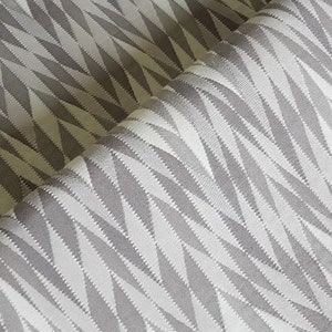Könnte beinhalten: Weißer und grauer Stoff mit Chevron-Muster. Der Stoff hat einen dezenten Glanz und eine strukturierte Oberfläche.