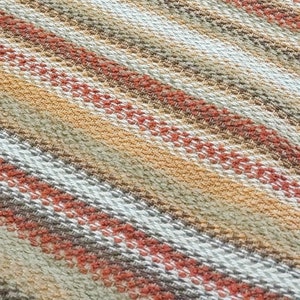 May include: Close-up of a woven fabric with a striped pattern in shades of beige, brown, and orange.