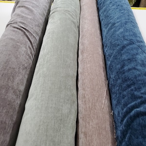 Pode incluir: Quatro rolos de tecido em diferentes cores: cinza, cinza claro, marrom e azul. O tecido tem uma superfície texturizada, ligeiramente felpuda.