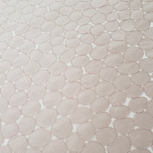 May include: A close-up of a pale pink fabric with a repeating pattern of embroidered circles.