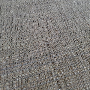 Puede incluir: Primer plano de una tela beige con un hilo plateado tejido en la tela. La tela tiene un brillo sutil.