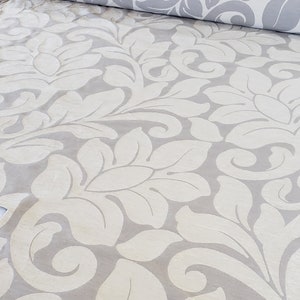 May include: A white and gray fabric with a damask pattern. The fabric has a raised texture and a subtle sheen.