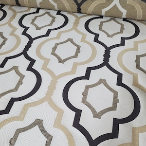 Puede incluir: Tela blanca con un patrón geométrico en negro y beige. El patrón presenta cuadrados y arcos entrelazados.