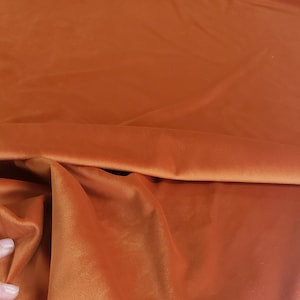 Pode incluir: Close-up de um tecido de veludo cor de ferrugem. O tecido é macio e tem um brilho sutil.