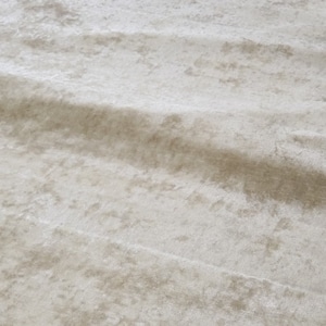 May include: A close-up of a white, textured fabric with a subtle sheen. The fabric has a soft, velvety feel and a slightly irregular surface.