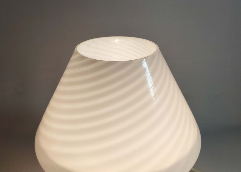 Pu&ograve; includere: Paralume per lampada in vetro bianco con un motivo a spirale. Il paralume ha una forma conica e una finitura liscia e lucida.