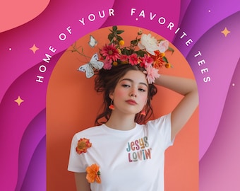 May include: A white t-shirt with the text 'JESUS LOVIN' printed in multicolored letters on the chest. The image features a person with flowers and butterflies in their hair, set against an orange background with a purple border and the text 'HOME OF YOUR FAVORITE TEES'.