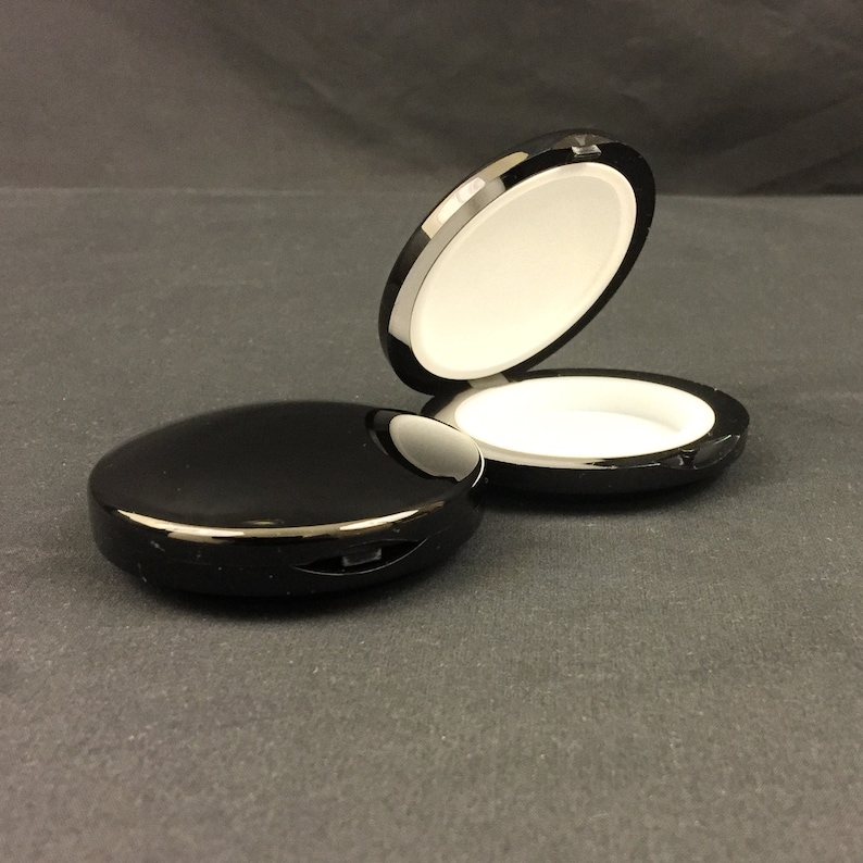May include: Two black round containers with white interiors. The containers are made of a glossy material and have a hinged lid.