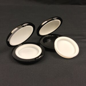 May include: Two black round containers with white lids. The containers are open and the lids are laying next to them.