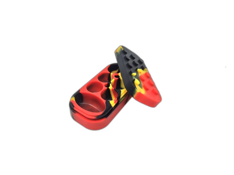 May include: A red, black and yellow silicone container with three compartments. The container is open and the lid is lying next to it.