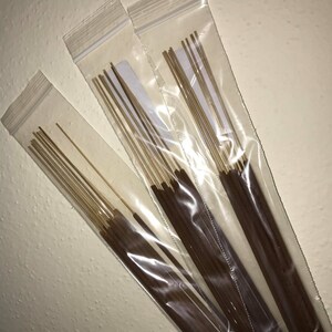 May include: Three packages of brown incense sticks in clear plastic bags. The sticks are bundled together and have a light brown color.