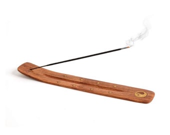 May include: A wooden incense burner with a yin yang symbol and stars carved into the surface. A black incense stick is burning and releasing smoke.