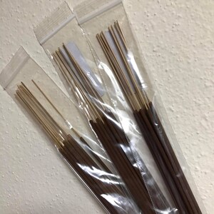 May include: Three clear plastic bags filled with brown incense sticks. The sticks are bundled together and have a natural wood color.