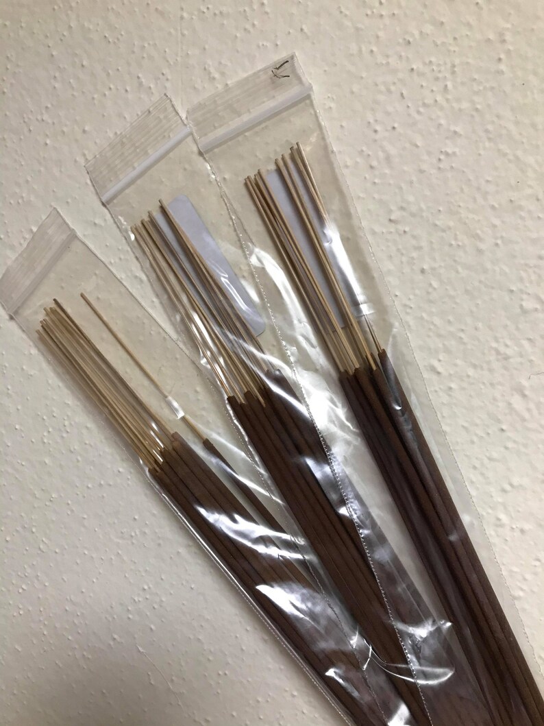 May include: Three clear plastic bags filled with brown incense sticks. The sticks are bundled together and have a natural wood color.