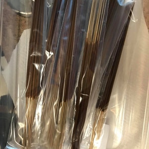 May include: Multiple bundles of brown incense sticks are packaged in clear plastic bags. The bags are stacked in a clear plastic container.