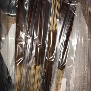May include: Multiple packs of brown incense sticks are bundled together in clear plastic bags. The bags are arranged in a clear plastic container.