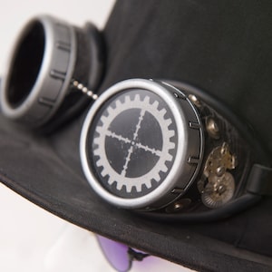 May include: A pair of black steampunk goggles with silver accents. The goggles have a gear design on the lenses and a black strap.