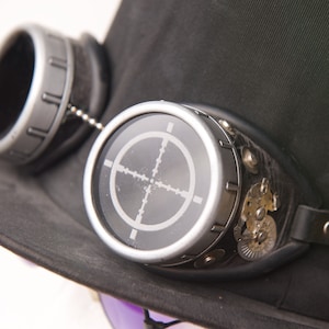 May include: A pair of silver steampunk goggles with a black leather strap and a target design on the lenses.