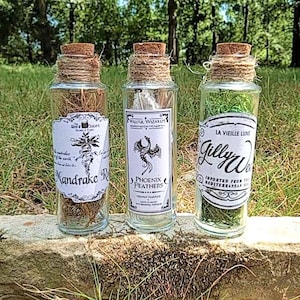 May include: Three glass bottles with cork stoppers and twine tied around the necks. Each bottle has a white label with black text and a graphic. The labels read "Mandrake Root", "Phoenix Feathers", and "Gillyweed".