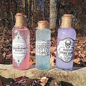 Könnte beinhalten: Drei Glasflaschen mit Korkstopfen und Schnur um die Hälse. Jede Flasche enthält eine andere farbige Flüssigkeit und hat ein Etikett mit einem Halloween-bezogenen Zaubertranknamen: "The Beautification Potion", "Invisible Elixir" und "Draught of Living Death".