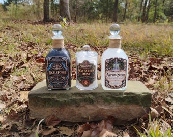 May include: Two glass bottles with spherical stoppers and twine-wrapped necks, and one glass jar with a lid. The left bottle is labeled Skeleforge, the center jar Wayfarer's Dust, and the right bottle Verum Serum, all by Blackthorne Apothecary Co.