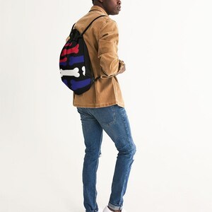 May include: A black drawstring backpack featuring a repeating horizontal pattern of stylized bones in red, white, and blue. The bag has black cord straps and is constructed from a soft fabric material with a rounded, flexible shape.