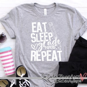 May include: A gray t-shirt with the text "Eat Sleep Grade Papers Repeat" in white with a pencil and heart graphic. The text is distressed and has a vintage look.