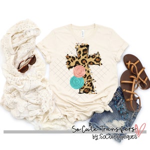 May include: A beige t-shirt with a leopard print cross and pink and blue floral accents. The text "So Cute Transfers by: SoCuteAppliques" is at the bottom of the image.