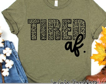 Puede incluir: Una camiseta verde con un diseño de estampado de leopardo que dice "TIRED af." en texto negro.