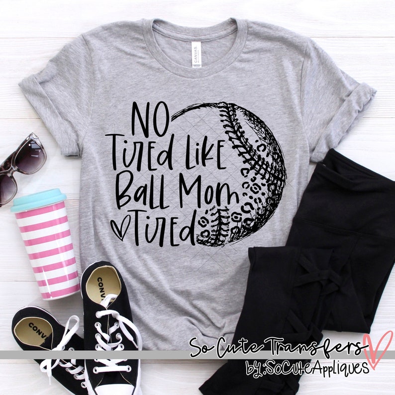 Op de afbeelding: Grijs T-shirt met een zwarte baseball-afbeelding en de tekst "NO Tired Like Ball Mom Tired".