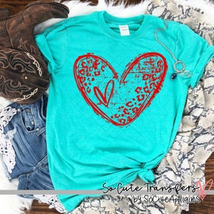May include: A turquoise t-shirt with a red heart design featuring a leopard print pattern. The heart is distressed and has a small heart inside. The text "So Cute Transfers by SoCuteAppliques" is at the bottom of the shirt.