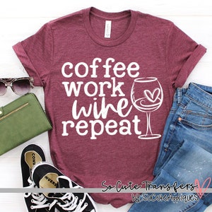 May include: A maroon t-shirt with the text "coffee work wine repeat" in white. A glass of wine with a heart in it is next to the text. The shirt is laid out on a white surface with a pair of black sneakers, a green wallet, and a pair of blue jeans.