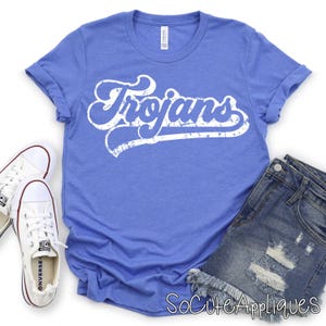 May include: A blue t-shirt with the word "Trojans" in white, retro-style lettering. The shirt is paired with denim shorts and white sneakers. The image is taken from a top-down perspective.