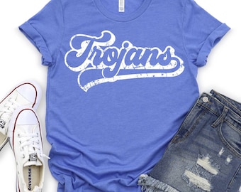 May include: A blue t-shirt with the word "Trojans" in white, retro-style lettering. The shirt is paired with denim shorts and white sneakers. The image is taken from a top-down perspective.