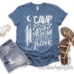 May include: A blue t-shirt with white text that reads "Camp tents, s'mores, fresh air, campfires, love". The shirt features a drawing of a tent and trees.