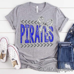 May include: A gray t-shirt with the word "PIRATES" in blue, outlined in black, and a black and white polka dot bow. White sneakers and blue jeans are visible.