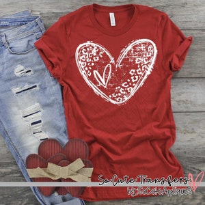 May include: Red t-shirt with a white distressed heart design featuring a leopard print pattern. The text "So Cute Transfers by SoCuteAppliques" is at the bottom of the shirt.