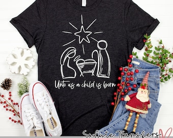 May include: A dark gray t-shirt with a white design of the nativity scene. The design includes a star, a manger, Mary, Joseph, and baby Jesus. The text "Unto us a child is born" is written below the design.