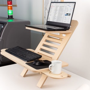 May include: A wooden laptop stand with a keyboard, mouse, and a white mug on a shelf. The stand is adjustable to different heights and angles.