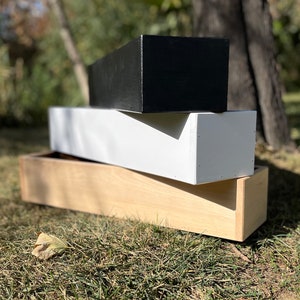 May include: Three wooden planter boxes stacked on top of each other. The top box is black, the middle box is white, and the bottom box is natural wood.