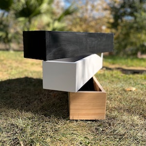 May include: Three wooden planter boxes stacked on top of each other. The top box is black, the middle box is white, and the bottom box is natural wood.