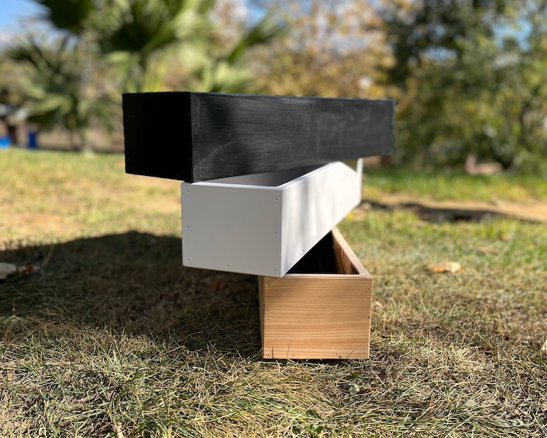 May include: Three wooden planter boxes stacked on top of each other. The top box is black, the middle box is white, and the bottom box is natural wood.