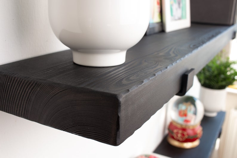May include: A black wooden shelf with a white bowl on top. The shelf has a rough, rustic edge and is mounted to a white wall.