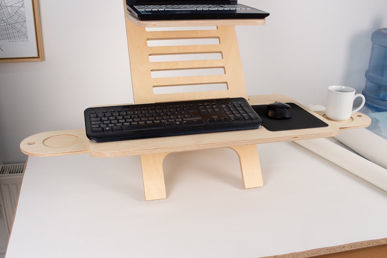 May include: A wooden standing desk with a black keyboard, mouse, and mousepad. There is a cup holder on the right side of the desk.