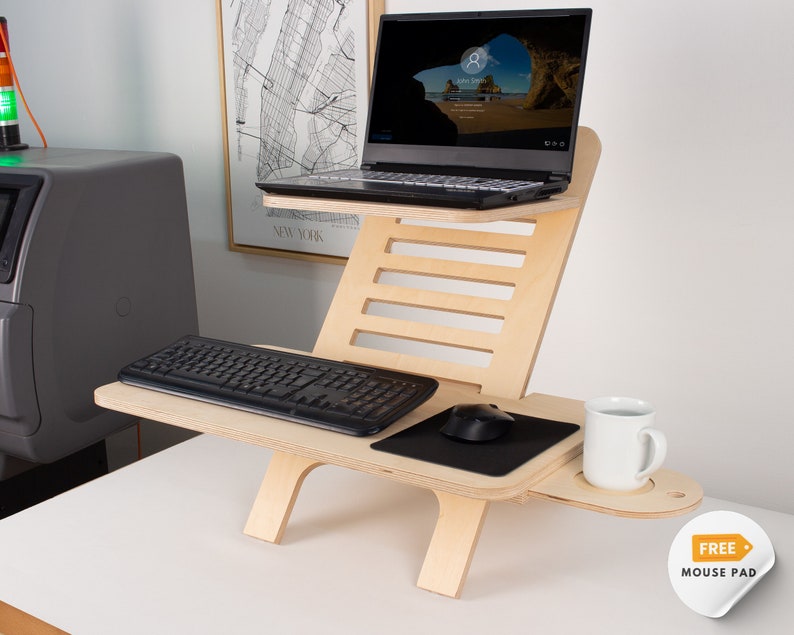 May include: A wooden standing desk converter with a laptop, keyboard, mouse, and a cup of coffee. The desk has a built-in mouse pad and a shelf for a cup.