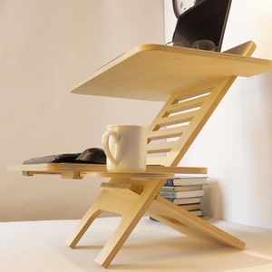 May include: A wooden laptop stand with a white ceramic mug and a black keyboard and mouse on the lower shelf. The stand is adjustable and has a natural wood finish.