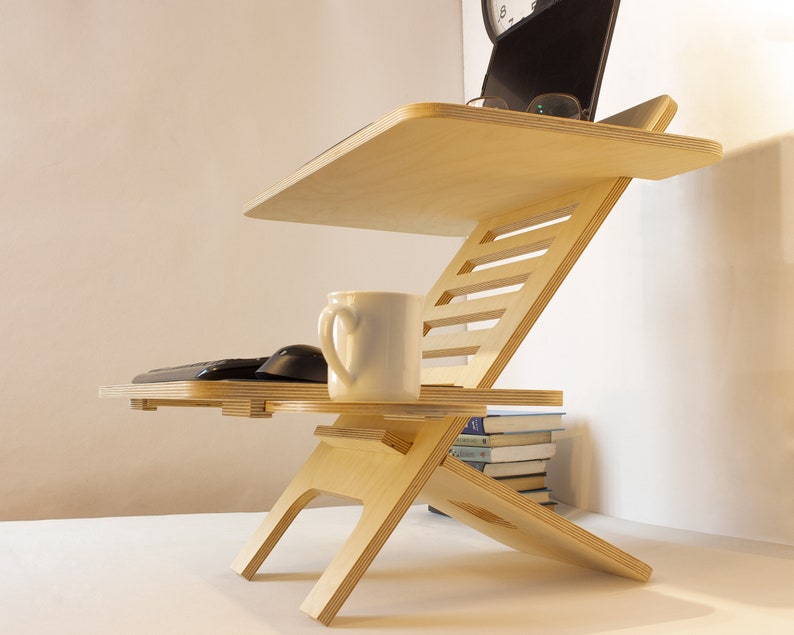 May include: A wooden laptop stand with a white ceramic mug and a black keyboard and mouse on the lower shelf. The stand is adjustable and has a natural wood finish.