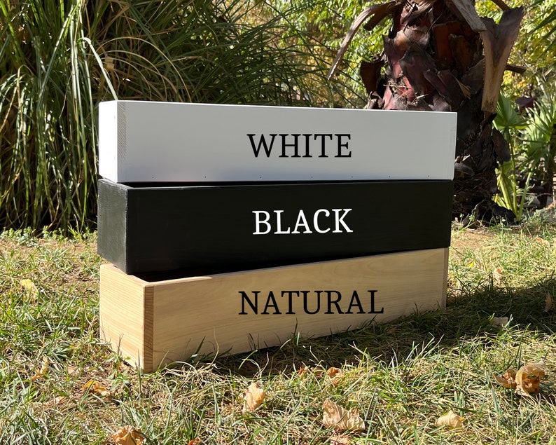 May include: Three wooden boxes stacked on top of each other. The top box is white with the word "WHITE" printed on it. The middle box is black with the word "BLACK" printed on it. The bottom box is natural wood with the word "NATURAL" printed on it.